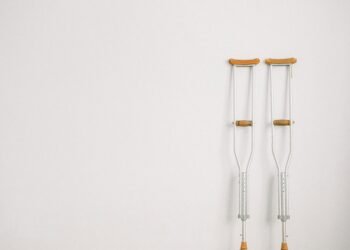 Minimalist image of a pair of crutches leaning on a white wall, symbolizing mobility aid.