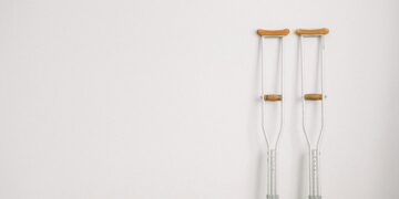 Minimalist image of a pair of crutches leaning on a white wall, symbolizing mobility aid.