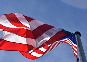 Close-up of a waving American flag under clear blue skies, symbolizing freedom and patriotism.