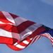 Close-up of a waving American flag under clear blue skies, symbolizing freedom and patriotism.