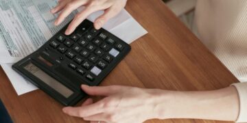 Close-up of a woman using a calculator and reviewing bills at home.