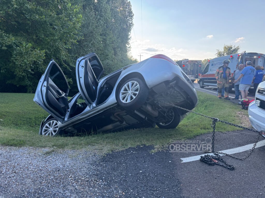 A silver 2014 Buick Verano rests nose-first in a ditch along McLey Highway (State Route 77/US 70A) near Thomas Lane in Carroll County, Tennessee, as emergency crews respond. Photo by Jesse Joseph, Carroll County Observer.
