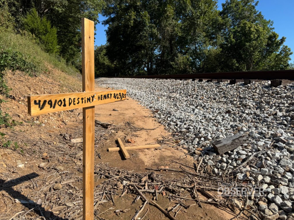 A wooden memorial cross inscribed with Destiny Henry’s name stands beside the CSX railroad tracks at the Harris Road crossing in Carroll County, Tennessee, marking the site of the August 13, 2025, fatal collision. Photo by Jesse Joseph/Carroll County Observer.