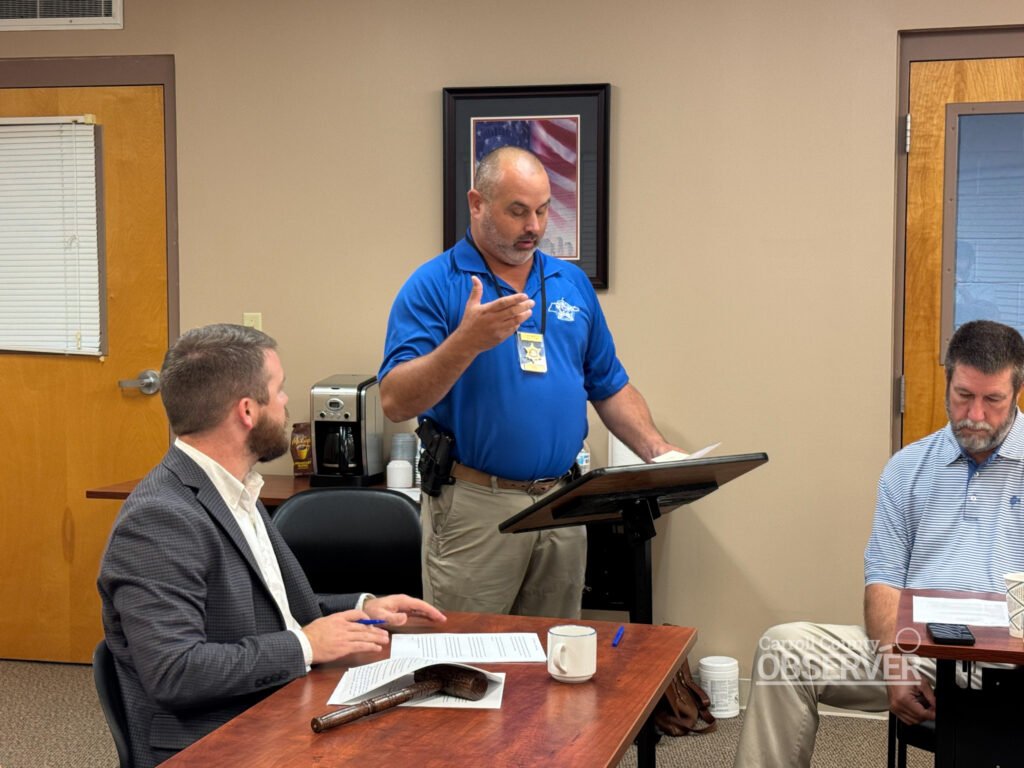 Chief Deputy Joel Pate speaks at a podium while Carroll County Mayor Joseph Butler listens at the Commission meeting. Pate explained that a diagnostic review is the first step toward safety improvements at the Harris Road railroad crossing. Photo by Jesse Joseph/Carroll County Observer.
