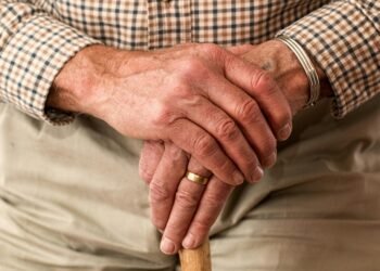A detailed image of elderly hands clasping a wooden cane, symbolizing aging and support.