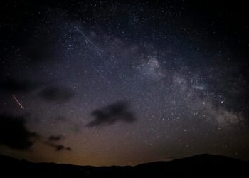 A stunning night sky showcasing stars, clouds, and the Milky Way galaxy with a visible meteor shower.
