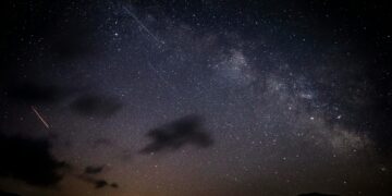 A stunning night sky showcasing stars, clouds, and the Milky Way galaxy with a visible meteor shower.