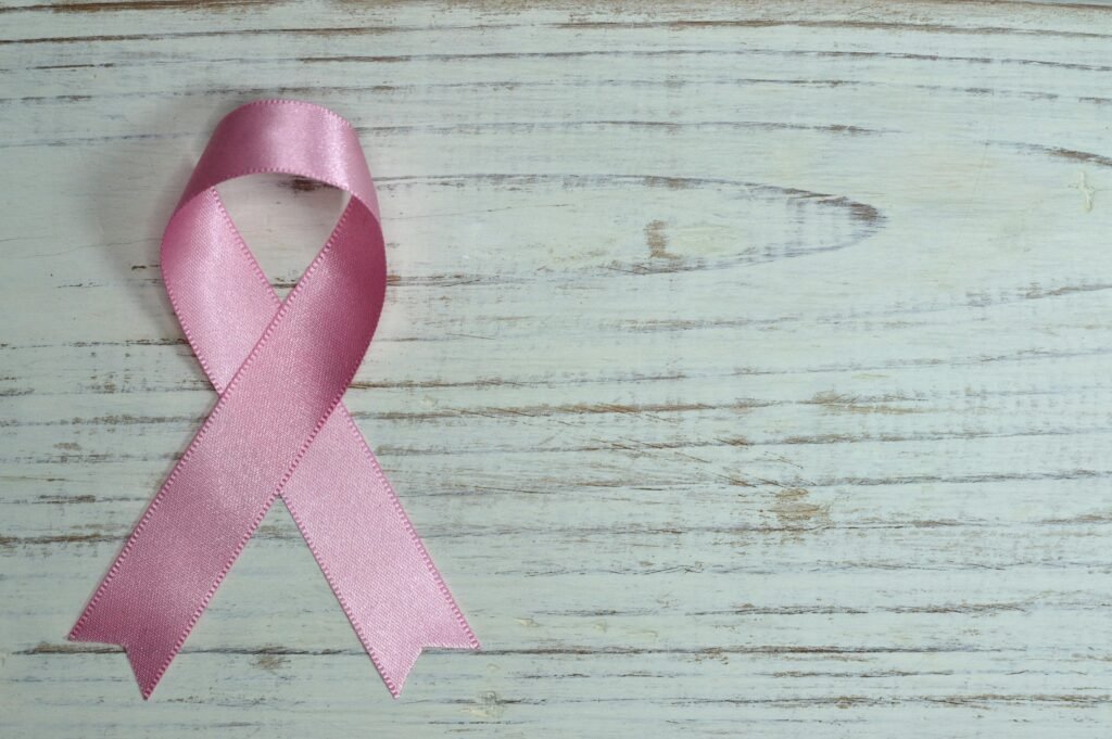 A pink ribbon symbolizing cancer awareness placed on a light wooden background.
