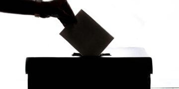 Silhouette of a hand placing a vote into a ballot box, symbolizing democracy.
