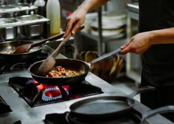 Chef preparing a dish with sautéed ingredients in a restaurant kitchen.
