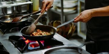 Chef preparing a dish with sautéed ingredients in a restaurant kitchen.