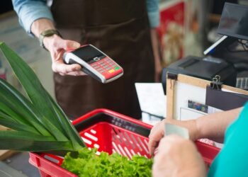 A customer using a contactless payment method at a grocery store checkout with fresh produce.