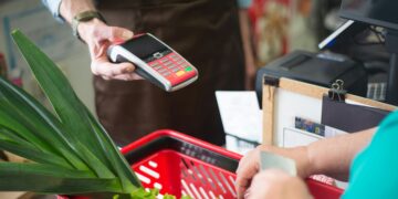 A customer using a contactless payment method at a grocery store checkout with fresh produce.