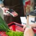 A customer using a contactless payment method at a grocery store checkout with fresh produce.