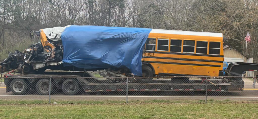 A heavily damaged yellow school bus covered with a blue tarp sits on a flatbed trailer after a fatal crash in Carroll County, Tennessee.
