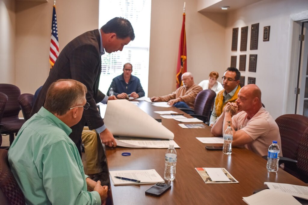 Dr. Jonathan Kee standing and showing architectural plans to Huntingdon Town Council members seated at a conference table.