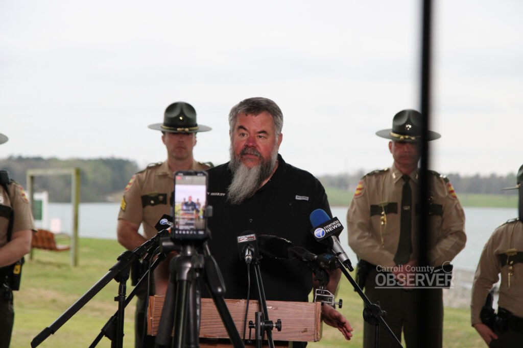 Carroll County Sheriff Andy Dickson speaks at a podium surrounded by Tennessee Highway Patrol troopers during a press briefing about a fatal school bus crash.