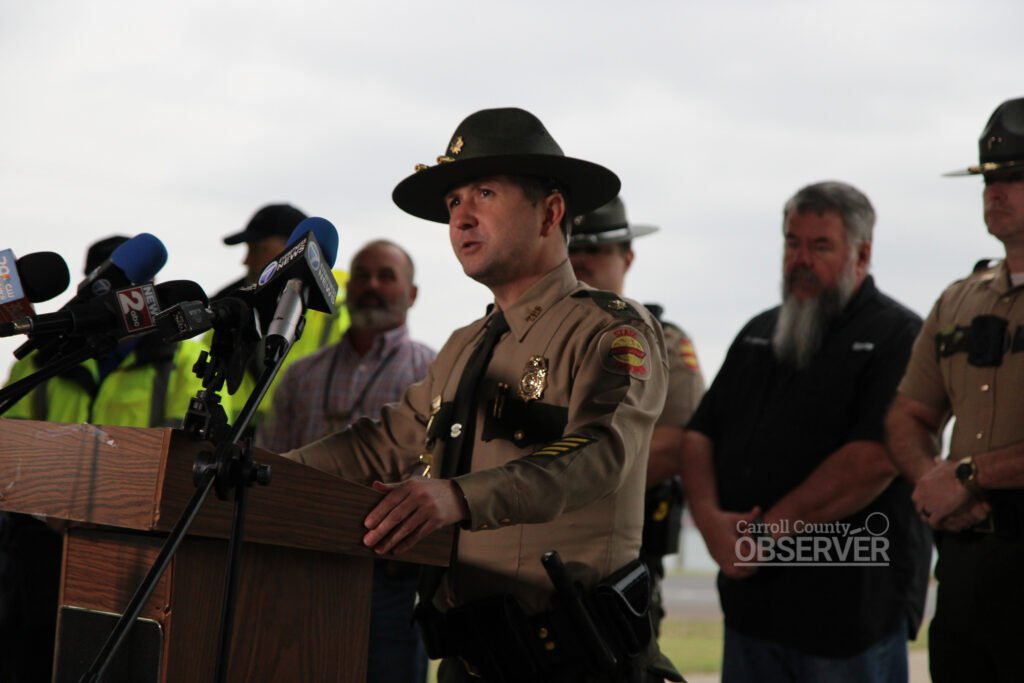 A Tennessee Highway Patrol sergeant in uniform speaks at a podium surrounded by law enforcement officials during a press briefing about a fatal Carroll County school bus crash.