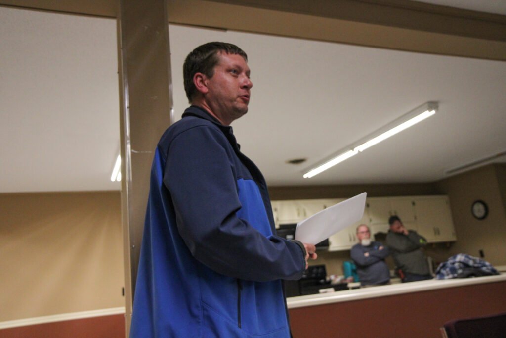 Derek Miller stands at the front of the room reading from a document during the Atwood town meeting.