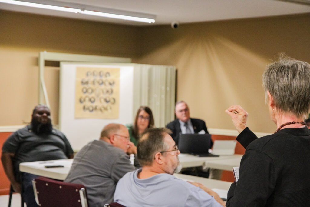 Joann Long faces the board with her fist raised while speaking, with aldermen and city staff visible in the background.