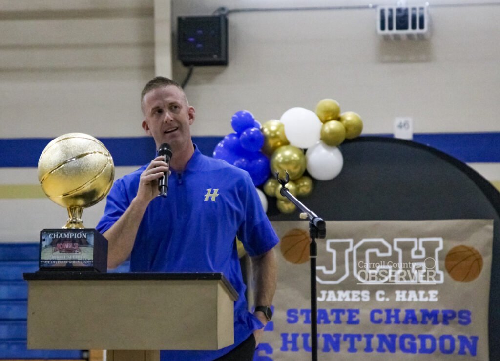 HMS Fillies head coach David Wilkins speaking at podium with state championship trophy during celebration ceremony.