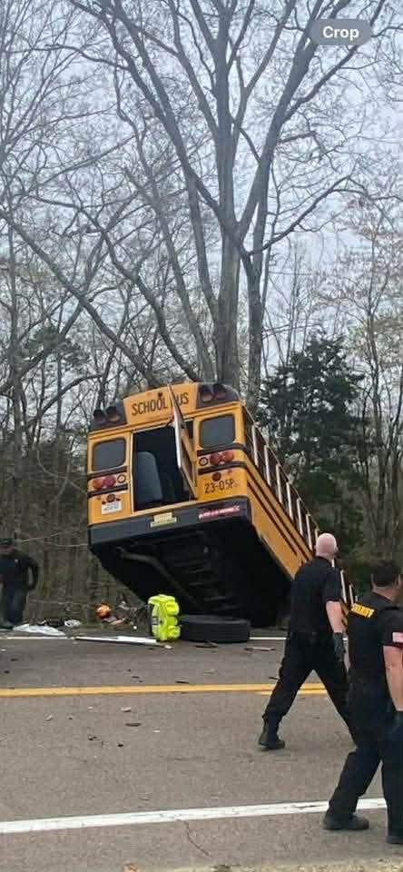 A yellow school bus stands nearly vertical on its rear end at a crash scene on Highway 70 in Carroll County as law enforcement officers walk nearby.