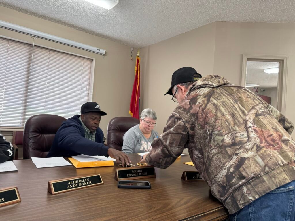 Hollow Rock Police Chief Tim Reeves leans over the board table to hand his retirement letter to Mayor Ronnie Webb.