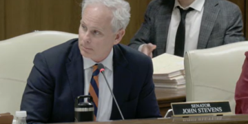 Sen. John Stevens sits at a committee table with his nameplate visible.