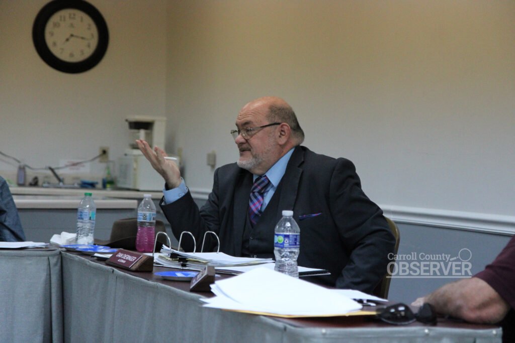 Alderman Dan Dieringer gesturing while speaking at Trezevant board meeting with nameplate visible in foreground.
