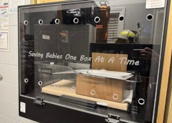 Interior of a Safe Haven baby box with a bassinet labeled "In Loving Memory of Cameron C. Scott" and a Tennessee kit inside.