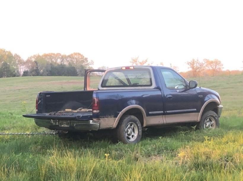 A 1997 blue Ford F-150 pickup truck parked in a grassy field.