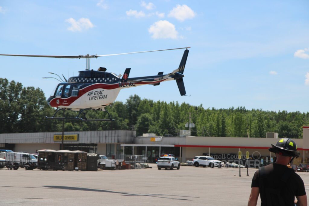 A firefighter in a yellow helmet watches an Air Evac Lifeteam helicopter lift off from a parking lot in Huntingdon, Tenn.